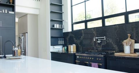 Modern kitchen featuring glossy white island, dark cabinetry, black marble backsplash