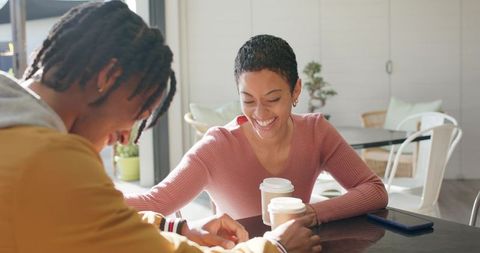 Diverse couple sharing takeaway coffee and laughing in cozy daytime cafe conversation
