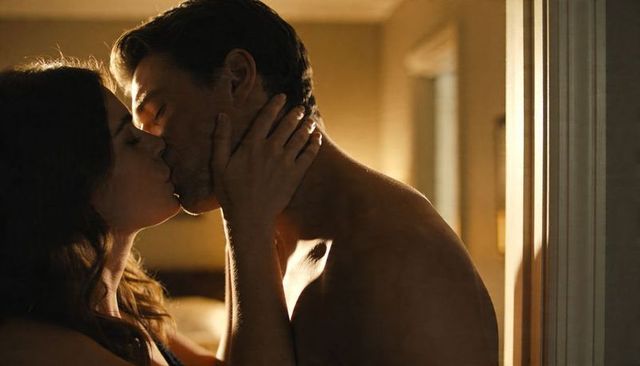 Intimate couple kissing in warm golden bedroom light shirtless man and woman embracing