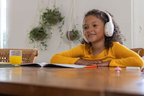 African american girl studying at home wearing headphones writing in notebook