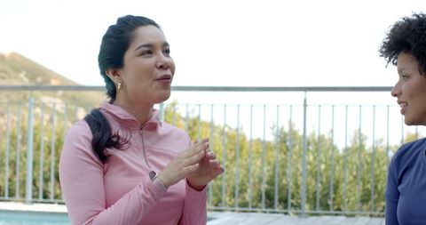 Women chatting on sunlit pool deck wearing athletic tops and smartwatch