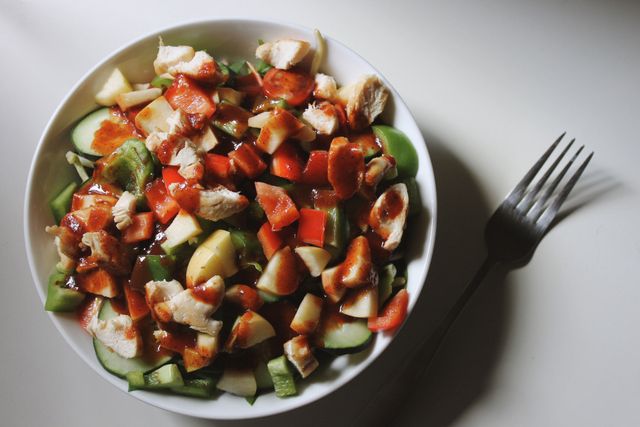Healthy chicken salad with fresh vegetables and dressing, perfect for promoting balanced diet and wholesome nutrition. Ideal for use in food and health blogs, recipe websites, or culinary magazines. Appeals to audiences looking for nutritious meal ideas or diet plans.