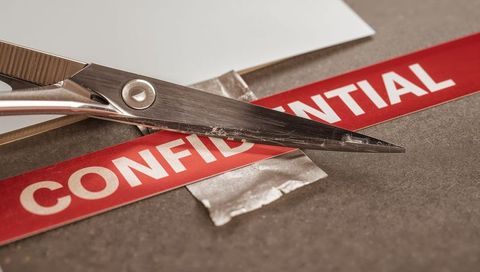 Scissors cutting confidential label on desk closeup showing torn tape and worn blades