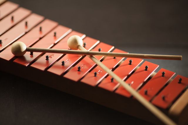 Close-up of a wooden xylophone with red keys, paired with two wooden mallets resting on it. Ideal for educational materials on music, musical instrument promotion, music classes, and percussion-focused content.
