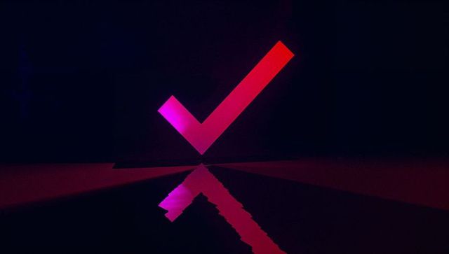 Neon gradient checkmark hovering on dark studio floor