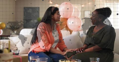 Friends sharing moment on sofa during intimate celebration with balloons and snacks