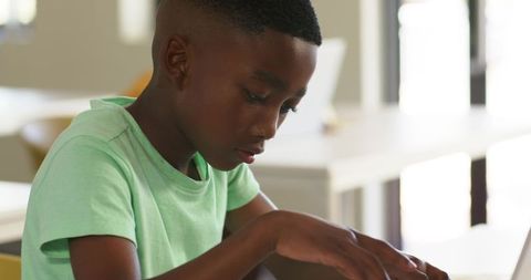 African American school-age boy studying and typing on laptop in bright classroom