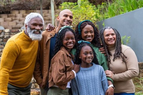 Diverse multigenerational family smiling together on garden terrace wearing knit sweaters