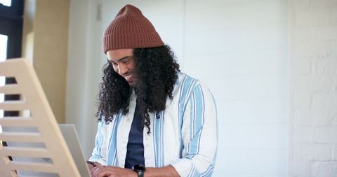 Mid-adult man wearing beanie typing on laptop in bright minimalist workspace, casual focus
