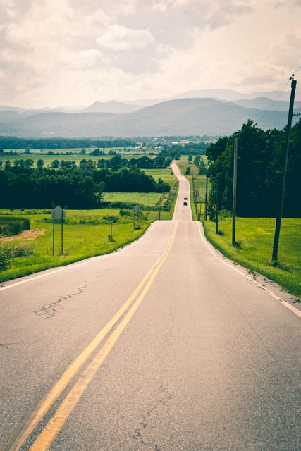 Long country road stretching into the distance with a scenic mountain view in the background. Wallpapers, travel blog, road trip themes, rural tourism promotions, and motivational posters.