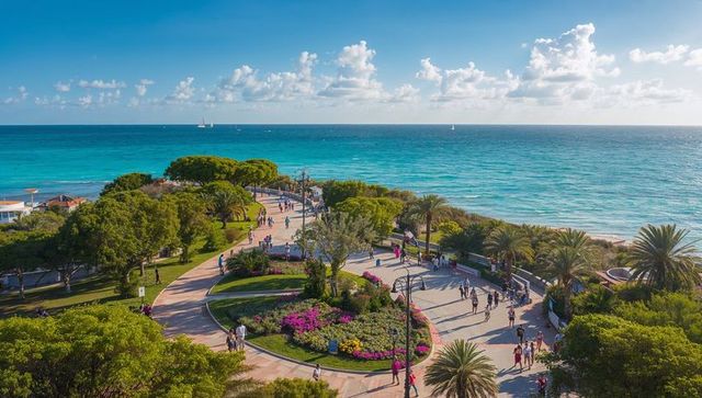 Sunlit oceanfront promenade with curving walkways, palm trees and flower gardens