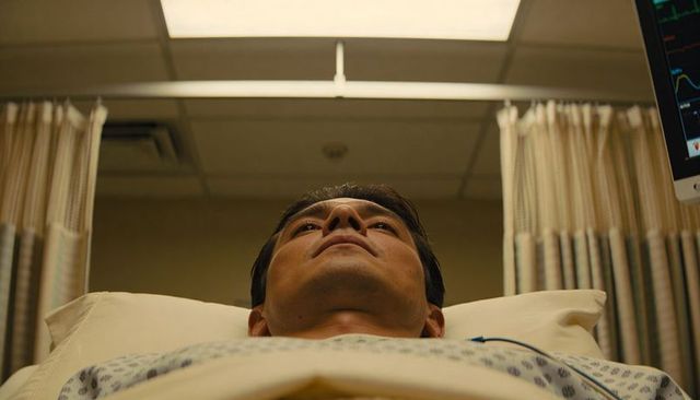 Adult male lying on hospital bed wearing gown with ecg leads in clinical treatment bay