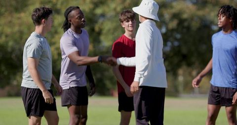 Youth sports coach shaking hands with players on grassy field before training session