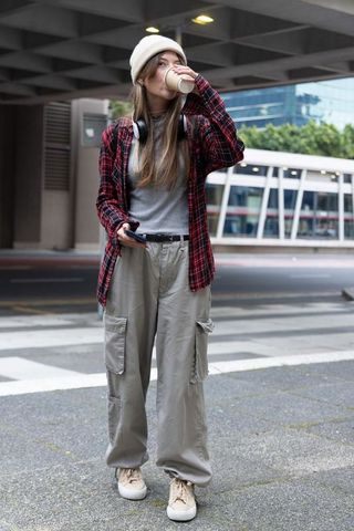 Young woman drinking coffee and checking phone standing on urban crosswalk underpass