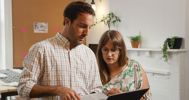 Caucasian couple reviews documents in an office setting. They are focused on work, collaborating on a project or task.
