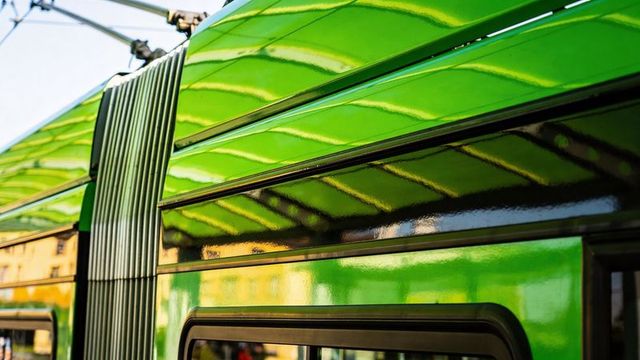 Glossy green tram exterior reflecting station canopy, accordion bellows and pantograph