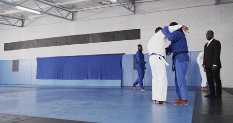 Men grappling in dojo, martial arts training in blue and white gis