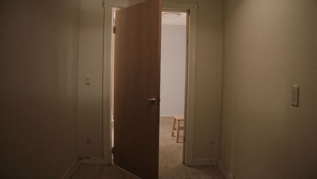 Partially opening wooden door revealing small room in narrow hallway with lever handle