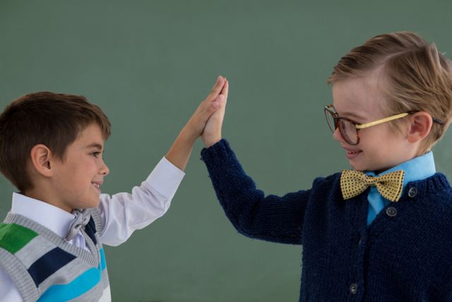 Two young boys dressed in formal business attire, including bow ties and glasses, giving each other a high five. This image can be used to represent themes of teamwork, success, collaboration, and childhood imagination. Ideal for educational materials, advertisements, and articles about child development or business concepts.