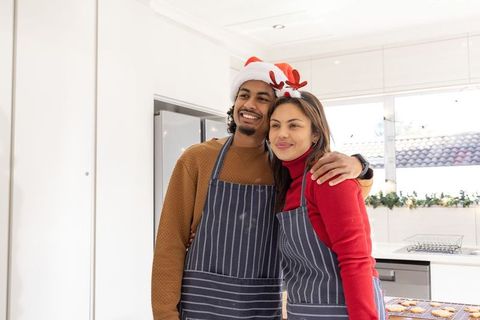 Diverse couple baking christmas cookies in striped aprons with santa hat and antlers