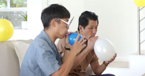 Asian men inflating balloons at home party celebration