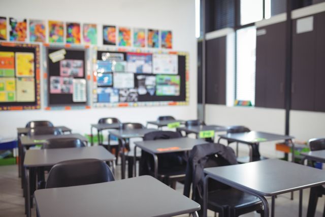 Empty classroom with neatly arranged desks and chairs, colorful posters on bulletin boards. Ideal for educational content, school brochures, academic presentations, and articles on education or teaching environments.