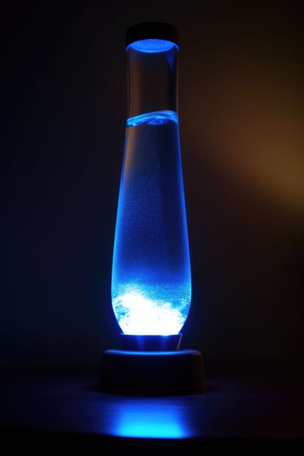 Blue lava lamp on table in dark room at night, created using generative ai technology. Retro, psychedelic, relaxation and interior decoration lamp concept digitally generated image.