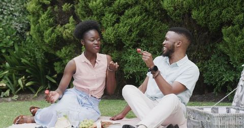 Young Couple Sharing Laughter and Snacks at Outdoor Picnic