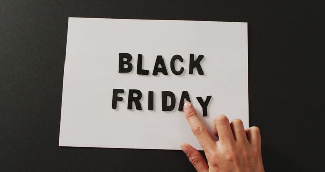 Hand moving black friday text in black letters on white rectangle with black background. Black friday, shopping, sale and retail concept digitally generated image.