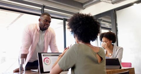 Team Collaboration: Man Leaning Over Table Presenting Budget Chart to Colleagues