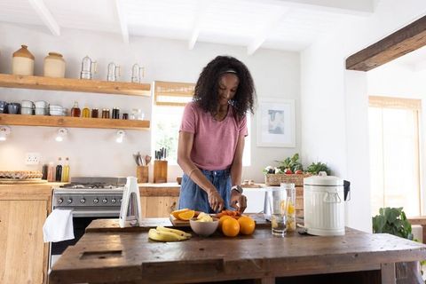 African american woman slicing oranges at rustic kitchen island preparing fresh fruit