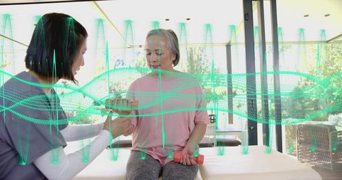 Therapist assisting senior woman lifting dumbbells during seated rehab session