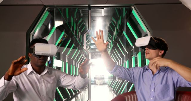 Two young men, one African American and one Caucasian, are engaged in a virtual reality experience, with copy space. They appear to be interacting with a digital environment, highlighting the growing trend of immersive technology in entertainment and education.