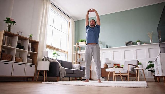 Man stretching barefoot in sunlit scandinavian living room blue tee gray sweatpants