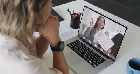 Woman Watching Laptop During Remote Presentation Holding Documents in Bright Workspace