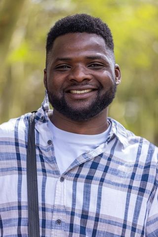 Smiling bearded man wearing plaid shirt and shoulder strap posing in forest casual headshot