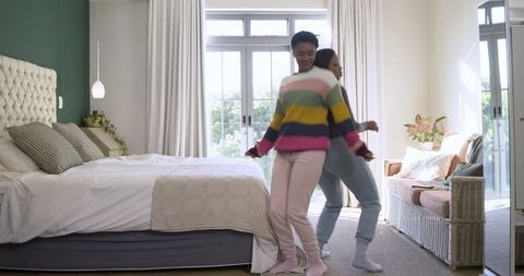 Joyful Friends Dancing Back-to-Back in Cozy Bedroom