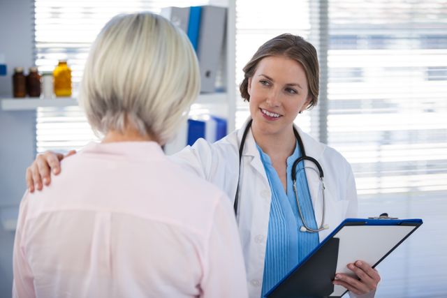 Female doctor consulting a mature patient in a medical office. Doctor wearing a stethoscope and holding a clipboard while smiling and talking to the patient. This image is useful for healthcare articles, medical websites, brochures on elderly care, and patient-doctor relationship material.
