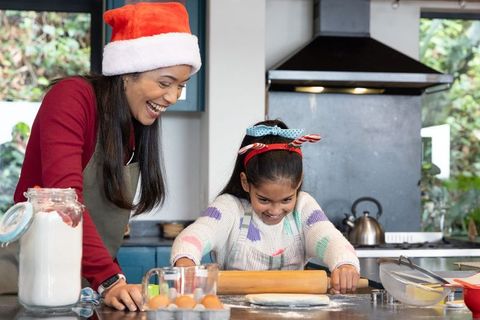 Asian mother and daughter joyfully baking christmas cookies in home kitchen, festive family