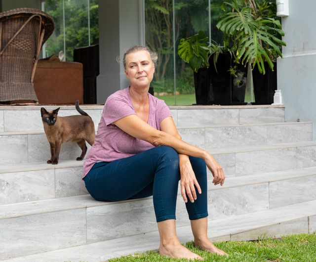 Thoughtful caucasian senior woman sitting by cat on steps outside house. unaltered, lifestyle, leisure, retirement, contemplation, pets.