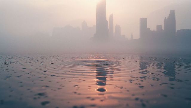 Tranquil Ripples with Misty Urban Skyline at Dawn