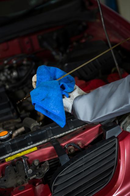 Mechanic checking the oil level in a car engine with a dipstick at repair garage