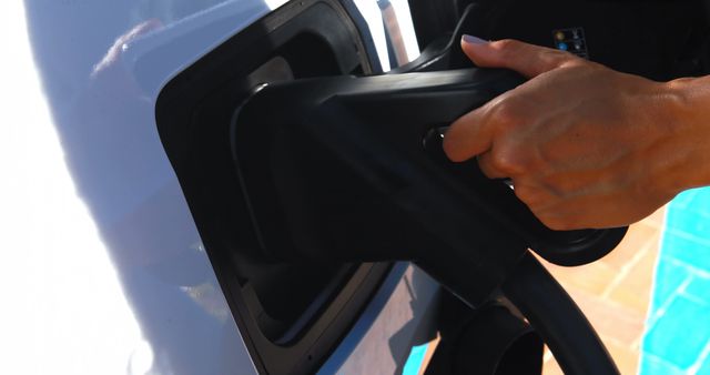 Close-up shows a person's hand plugging an EV charger into an electric vehicle. Useful for promoting sustainable energy, renewable energy solutions, advertisements for electric cars, and clean transportation initiatives.