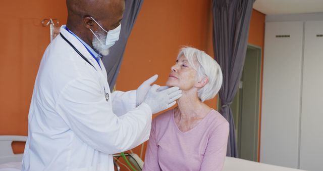 A doctor wearing a mask and gloves performs a medical exam on a senior woman, gently examining her neck. The setting appears to be a clinical environment. Useful for topics related to medical checkups, elderly care, healthcare services, doctor consultations, and healthcare professionalism.