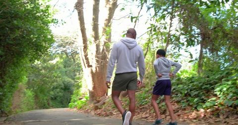 African american man and boy walking wooded trail wearing hoodies and sneakers