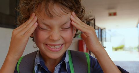 Stressed schoolboy rubbing temples in school hallway
