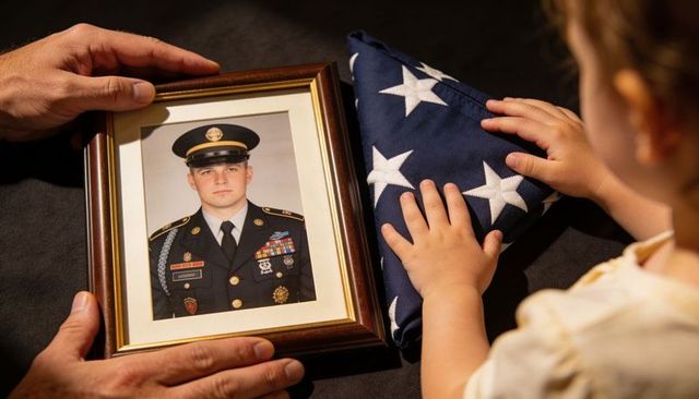Family honoring fallen soldier: child touching folded us flag beside framed portrait