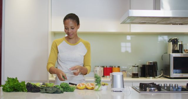 Woman is preparing a healthy meal using fresh vegetables and fruits in a modern kitchen. She is smiling while cutting ingredients, contributing to a theme of healthy living and cooking at home. This image is ideal for use in content related to healthy recipes, cooking tutorials, kitchen appliances, nutrition blogs, and lifestyle magazines.