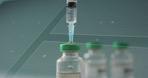 Withdrawing medication from glass vial with green cap, syringe tip showing droplet, sterile