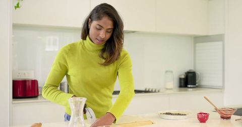 Indian woman baking pastry on modern kitchen island in lime sweater